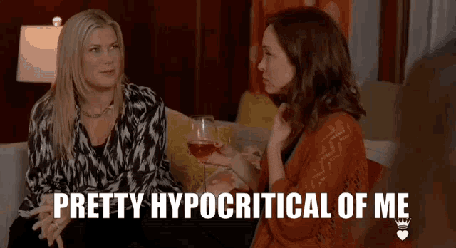 two women are sitting on a couch holding wine glasses and one of them is saying pretty hypocritical of me .