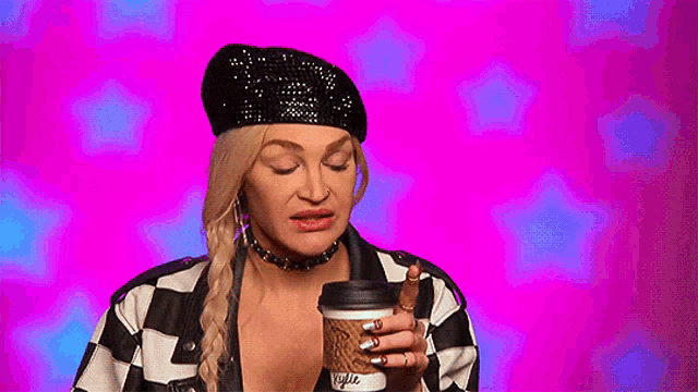 a woman wearing a beret and a checkered jacket is holding a coffee cup .