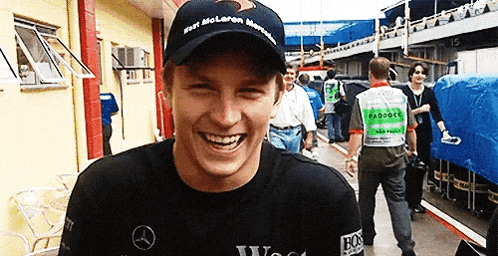 a man wearing a mclaren hat is smiling while standing in front of a group of people .