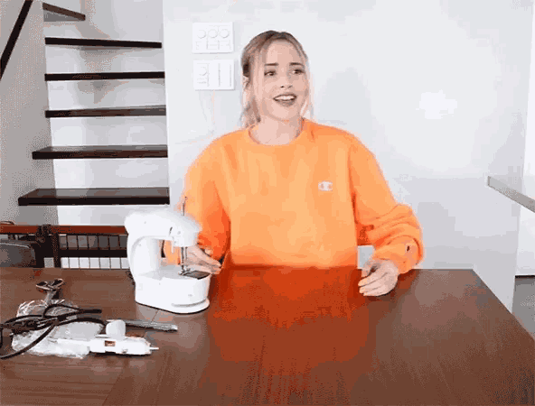 a woman wearing an orange champion sweatshirt is sitting at a table with a sewing machine .