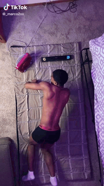 a shirtless man is laying on a bed with a fan and a tiktok watermark