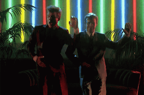two men are dancing in front of neon lights