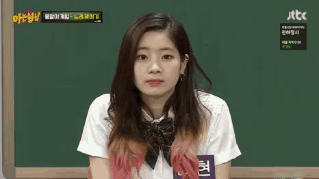 a girl in a school uniform is sitting in front of a blackboard with a question mark on it