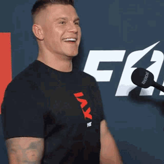 a man in a black t-shirt is smiling in front of a sign that says rode
