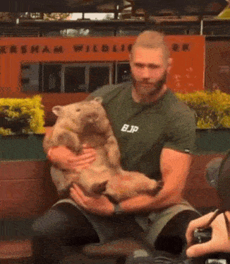 a man is holding a wombat in his arms while wearing a bjp shirt
