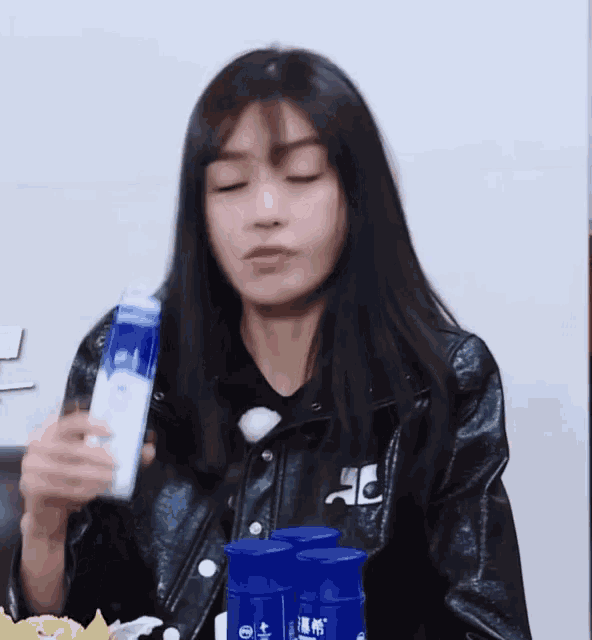 a woman in a black leather jacket is holding a bottle of milk .