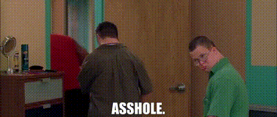two men standing next to each other in a room with the words asshole written on the wall .