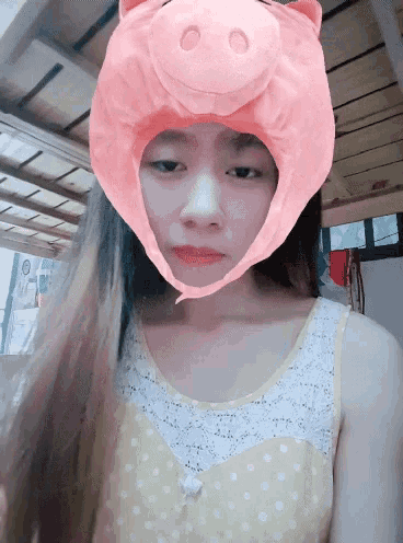 a girl wearing a pink pig hat looks down at something