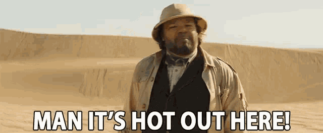 a man in a hat and trench coat is standing in the middle of a desert .