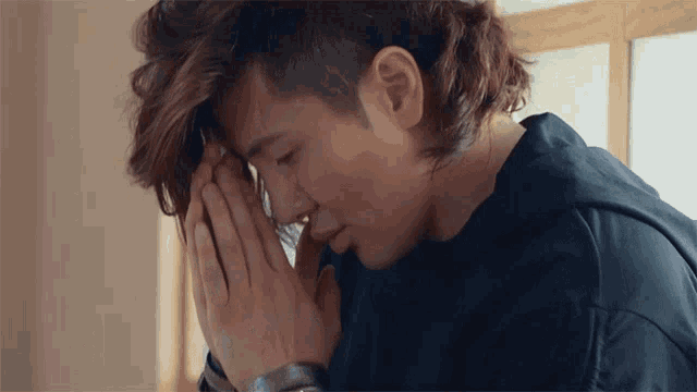 a man with his hands folded on his face looks down