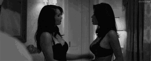 two women in lingerie are standing next to each other in a room and looking at each other .