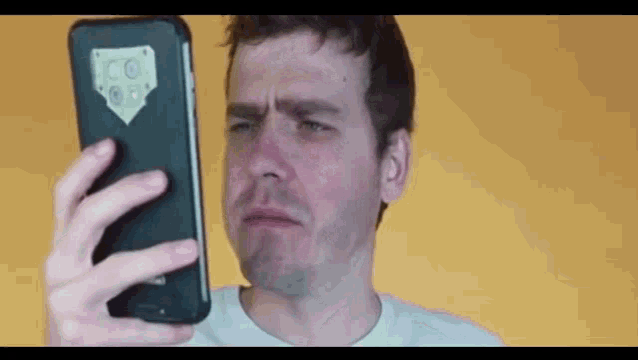 a man is making a funny face while looking at his cell phone .