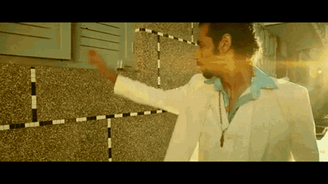 a man in a white suit and blue shirt is standing in front of a brick wall