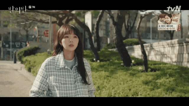 a woman in a plaid jacket is walking down a street with trees in the background