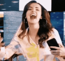 a woman is laughing while holding a cell phone and wearing hoop earrings .