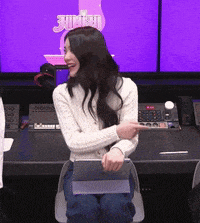 a woman is sitting at a desk with a purple screen behind her that has the word jump on it