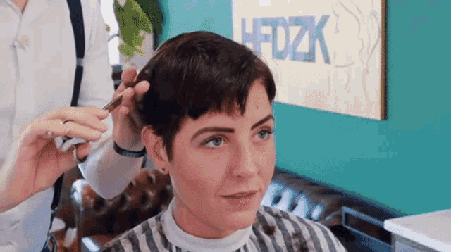 a woman is getting her hair cut by a barber in front of a sign that says hfdzk