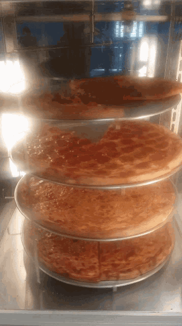 several pizzas are stacked on top of each other in a glass case