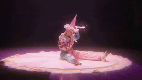 a woman in a clown costume is sitting on a stage holding a microphone
