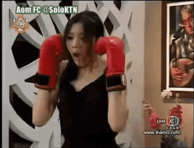 a woman wearing red boxing gloves is on a tv screen with a caption that says aom fc @soloktn