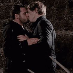 two men are hugging and kissing in front of a hay bale .