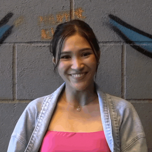a woman wearing a pink top and a denim jacket smiles