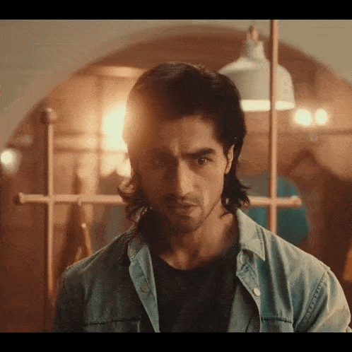a man with long hair is wearing a denim jacket and black shirt
