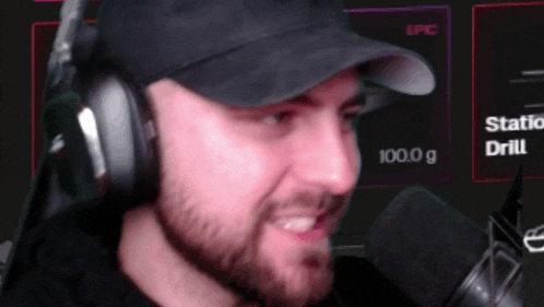 a man wearing headphones and a hat is talking into a microphone with a screen behind him that says station drill