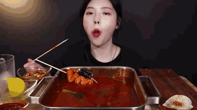 a woman is eating food with chopsticks in a pot of sauce