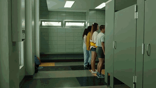 a group of people are standing in a hallway in front of green stalls