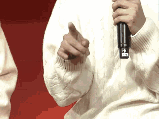 a person in a white sweater is holding a microphone and pointing at it .