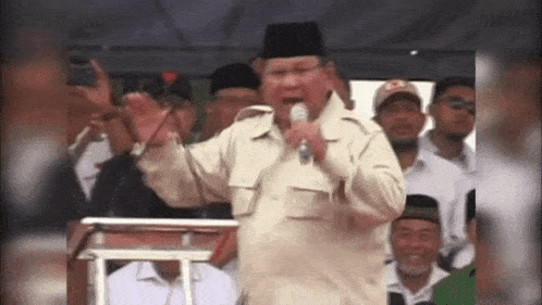 a man is speaking into a microphone while standing in front of a crowd of people .