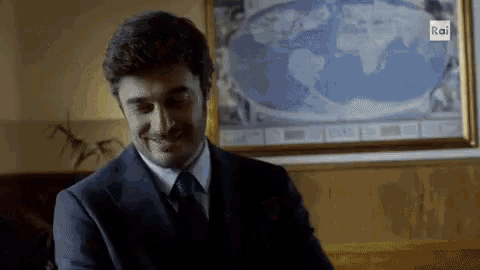 a man in a suit and tie is smiling in front of a picture of a map of the world ..