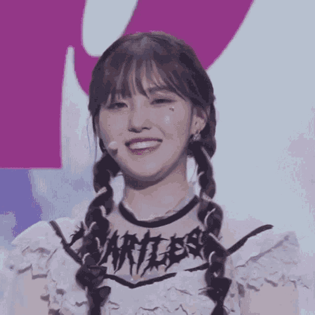a young woman with pigtails is smiling and wearing a white shirt with a black graphic on it .