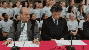 two men are sitting at a table with microphones and one of them has a shirt on that says ' aoc '