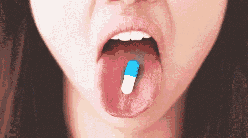 a woman is sticking out her tongue while taking a blue and white pill .