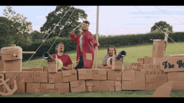a group of men are standing in front of a cardboard ship that says " i be pirate "