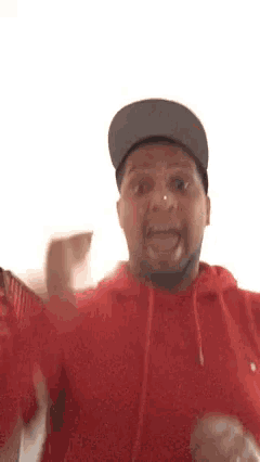 a man wearing a hat and a red hoodie making a funny face