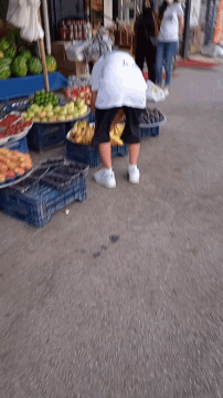 a person standing in front of a fruit stand with a sign that says ' vegetables '