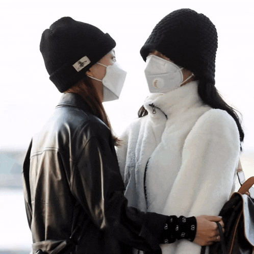 two women wearing face masks and hats are hugging