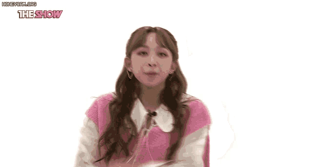 a woman in a pink vest and white shirt is standing in front of a white background with the show written on it