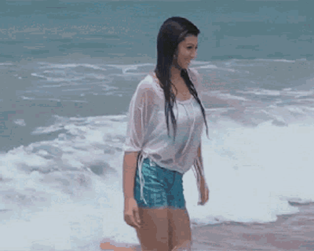 a woman in a white shirt and blue shorts is walking on the beach
