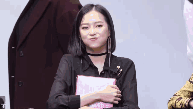 a woman wearing a choker and earrings holds a pink book in her hand