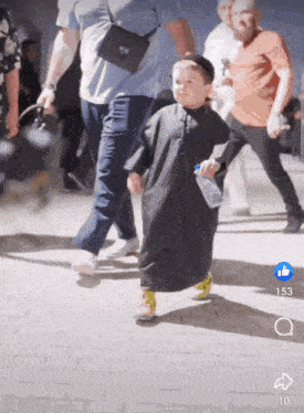a little boy in a black robe is walking with a bottle of water