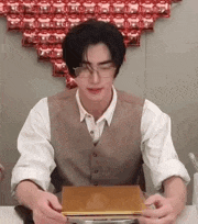 a man in a vest and glasses is sitting at a table holding a piece of paper .