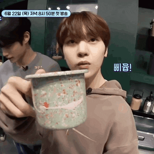 a young man is holding a cup with korean writing on the bottom