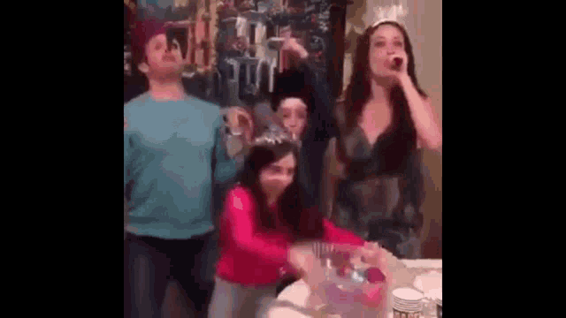 a group of people are standing around a table drinking and dancing .