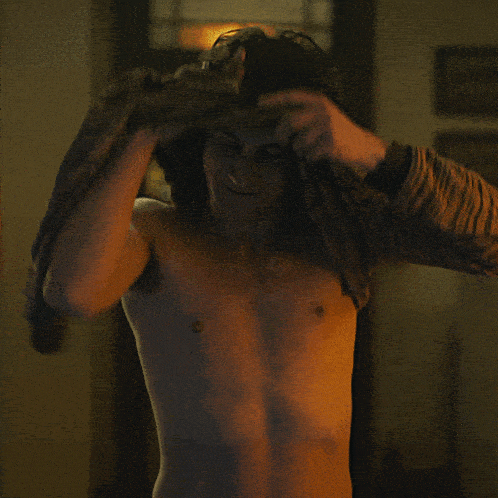 a shirtless man stands in a dark room