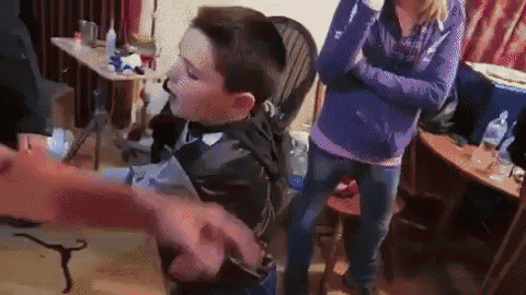a group of people are standing around a boy in a chair .