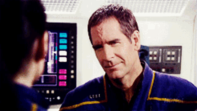 a man in a blue shirt with a yellow stripe on the sleeve is looking at another person